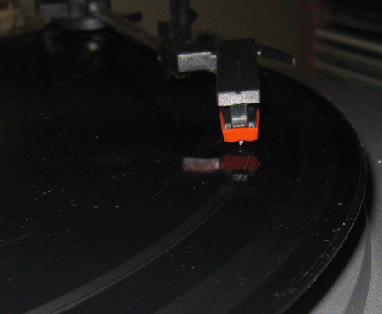 Photo slideshow shows a stylus turning the black grooves of a record gray as it plays. Last frame shows a close-up of the stylus which is bent to the left.
