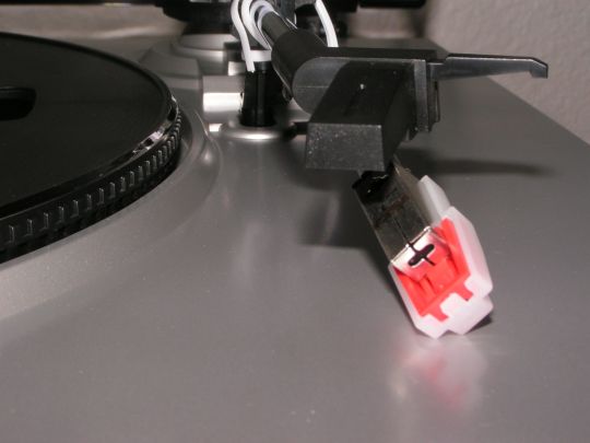 Close-up photo shows the cartridge and stylus unit laying on the plastic turntable plinth (body).