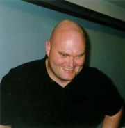 Photo shows Roger Binns' smiling and slightly bowing, showing his bald head.