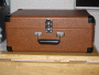 Photo shows the Crosley CR249 turntable on a table. The cover is closed. A carrying handle is visible.